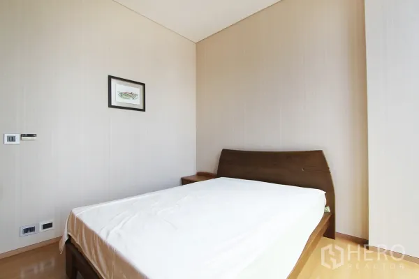 Condominium for sale in Bang Rak, Bangkok - Bright minimalist bedroom in a Bangkok condo with wood bedframe, neutral walls and framed art.