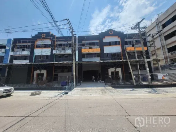 Factory for rent or sale in Samut Prakan - Front elevation of modern black-and-orange industrial building with driveway and gates.