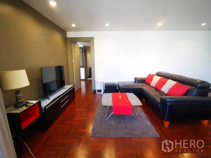 Condominium for rent in Khlong Toei, Bangkok - Living room featuring black leather sectional sofa, TV console and red accent decor.