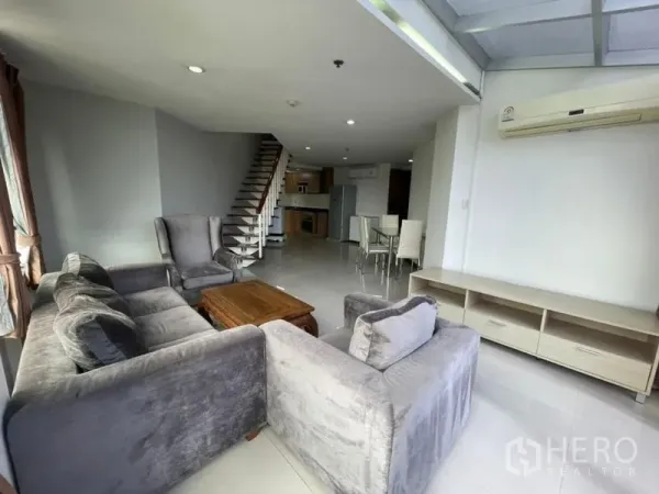 公寓 出租在Khlong Toei, Bangkok - 曼谷空堤区开放式客厅，灰色转角沙发、木质茶几、室内楼梯、餐区与厨房，临近BTS蓬蓬站。