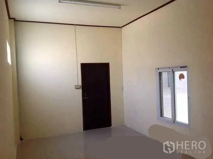 Factory for rent in Mueang Nakhon Pathom, Nakhon Pathom - Compact internal office with white walls, a sliding window and a dark door inside the factory.