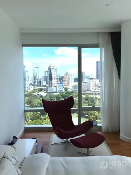 公寓 出租或出售在Pathum Wan, Bangkok - 卧室一角的红色躺椅，俯瞰隆比尼公园与天际线