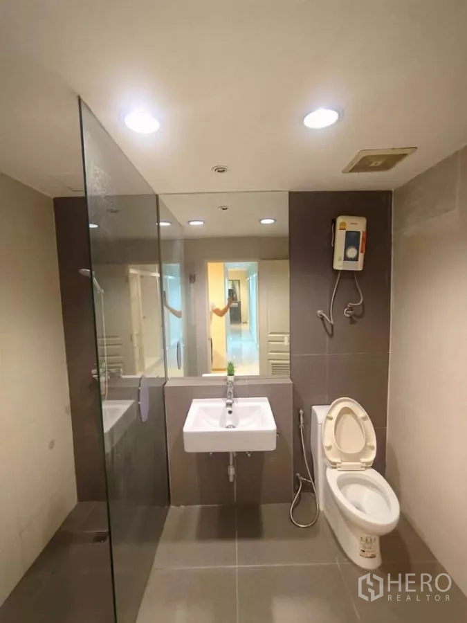 Condominium for rent in Khlong Toei, Bangkok - Modern bathroom with glass-enclosed shower, wall-mounted sink, and toilet.