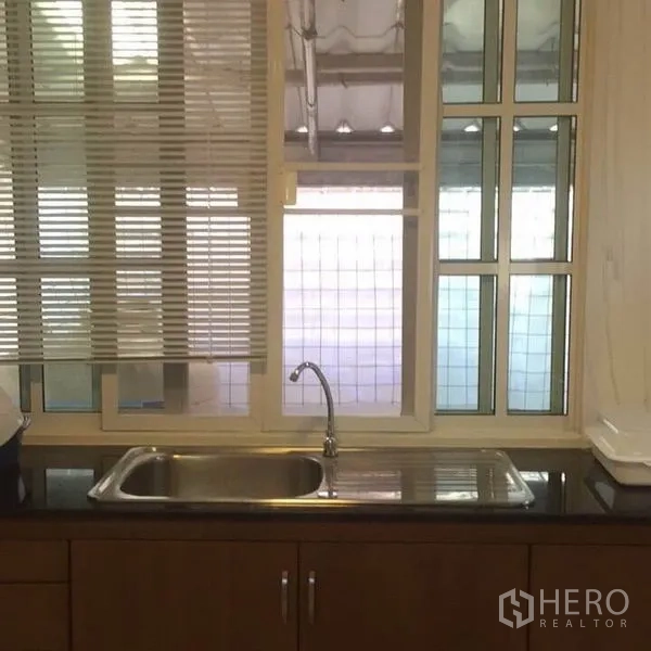 Townhouse for rent in Bang Kapi, Bangkok - Kitchen sink below a large window with blinds and dark granite countertop.