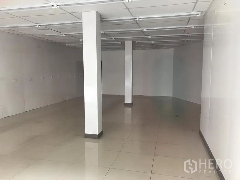 Retail Space for rent in Khlong Toei, Bangkok - Empty ground-floor retail unit with white walls, glossy tiled floor, support columns and a suspended grid ceiling with fluorescent light tracks.