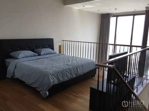 Condominium for rent in Khlong Toei, Bangkok - Spacious loft bedroom with king-size bed, railing and large windows with city light.