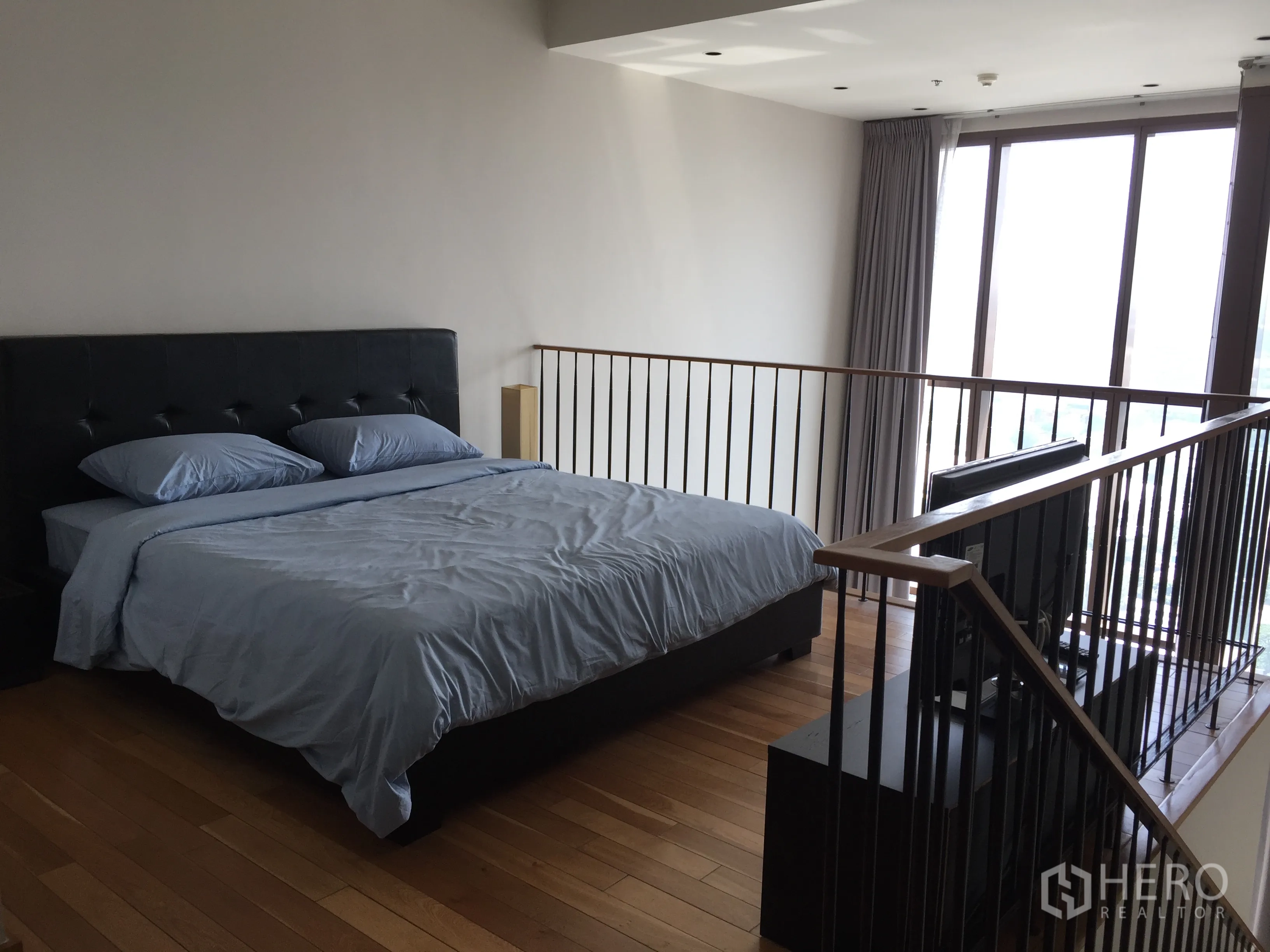 Condominium for rent in Khlong Toei, Bangkok - Spacious loft bedroom with king-size bed, railing and large windows with city light.
