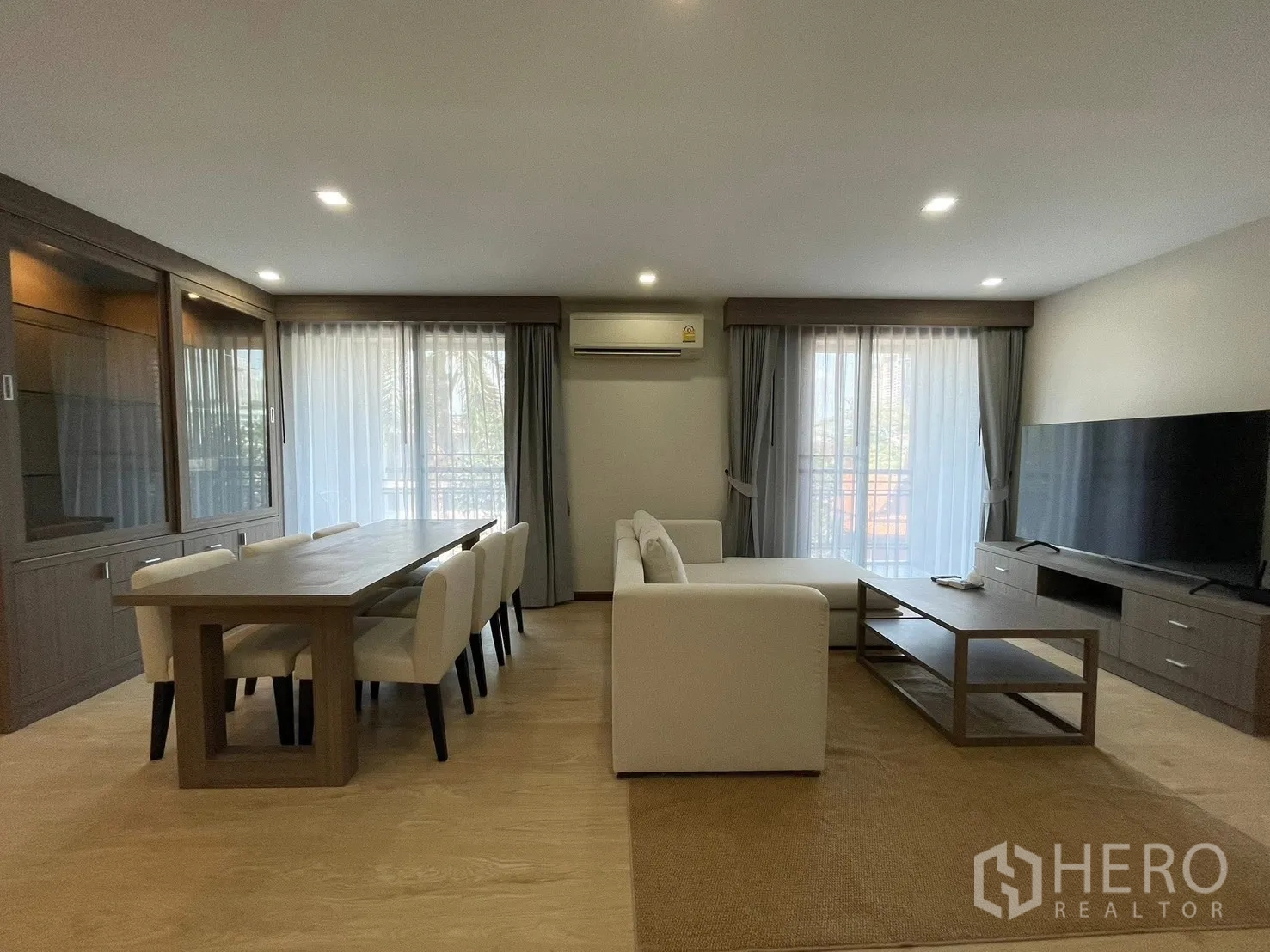 คอนโด for rent in Watthana, Bangkok - มุมรับประทานอาหารสำหรับแปดที่นั่งข้างโซฟาสีขาวและชั้นวางทีวี มีหน้าต่างบานกว้างพร้อมม่านโปร่ง
