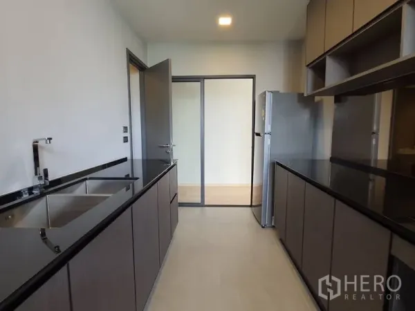 Condominium for sale in Huai Khwang, Bangkok - Sleek galley kitchen featuring black stone countertops, double sink and full-height cabinetry.