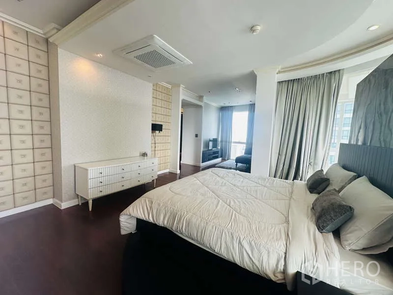 Condominium for rent or sale in Khlong Toei, Bangkok - Spacious master suite with king bed on a curved platform, seating nook and dark wood floors by tall windows.