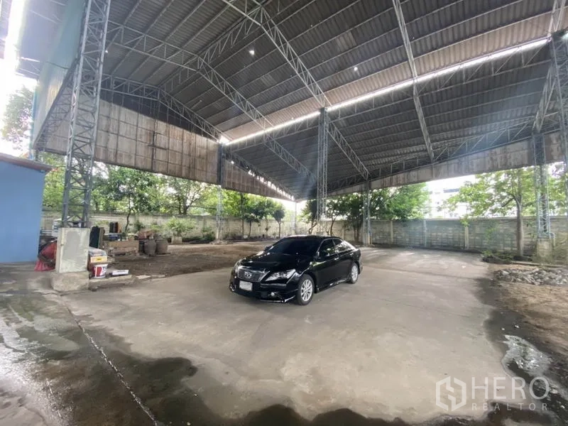 Warehouse for rent in Suan Luang, Bangkok - Open-air warehouse bay with metal roof and large maneuvering area for trucks.