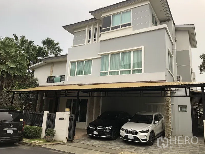 Detached House for rent or sale in Saphan Sung, Bangkok - Angled view of grey detached house with wide windows and metal awning over parking