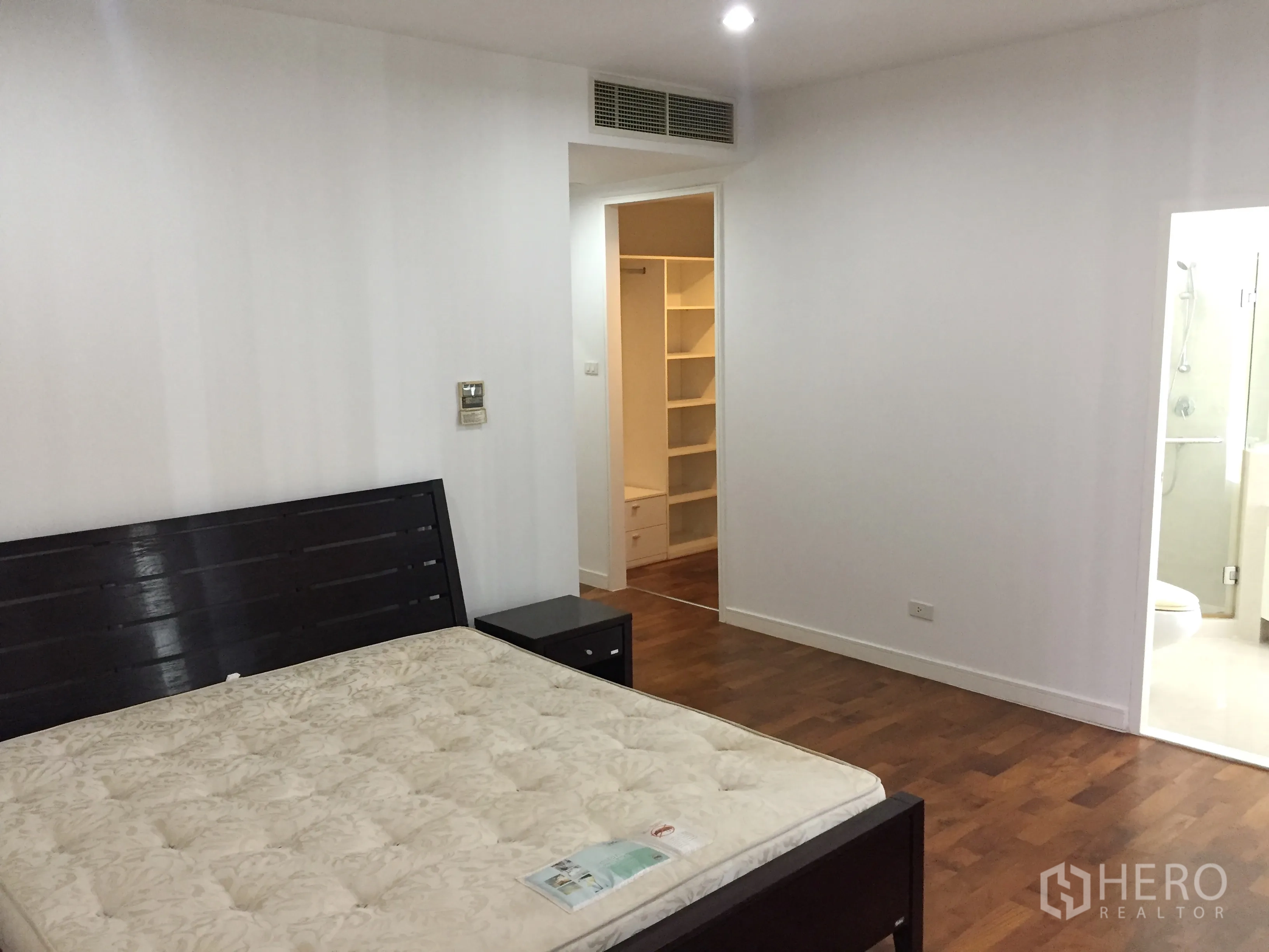 Condominium for rent in Khlong Toei, Bangkok - Master bedroom with wood flooring leading to a walk-in closet and en-suite bathroom.