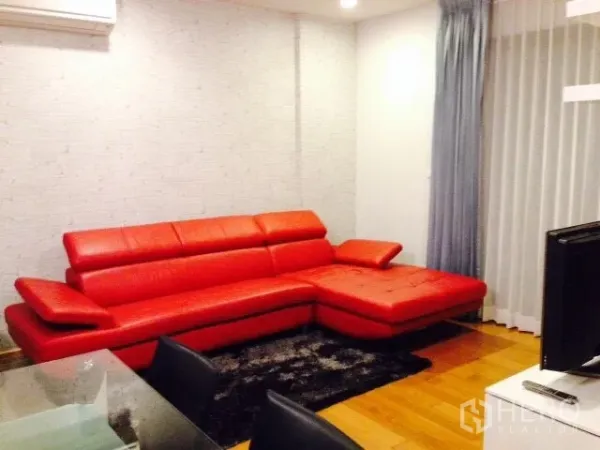 Condominium for rent in Phaya Thai, Bangkok - Modern living room with a striking red leather sectional sofa, wood floors, and sheer curtains in a Phaya Thai condo.