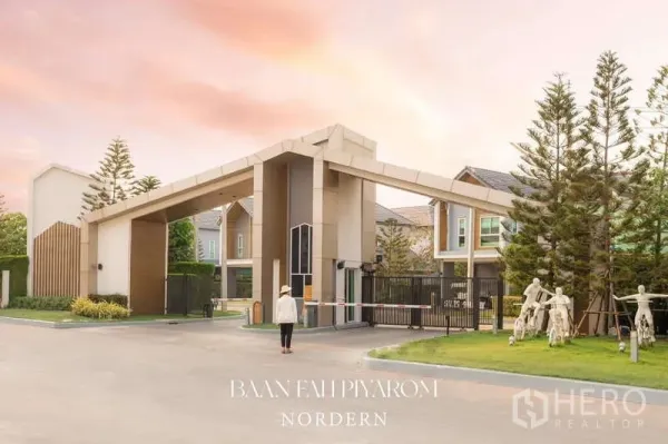 Detached House for sale in Lam Luk Ka, Pathum Thani - Secure gated entrance of an upscale housing estate with tall trees at sunset.