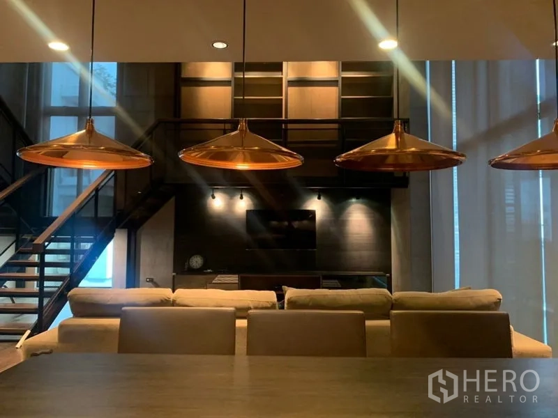 公寓 出租在Watthana, Bangkok - 阁楼风客厅，餐桌上方铜色吊灯，沙发与电视墙。
