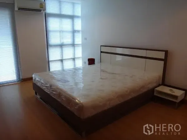 Condominium for rent in Bang Rak, Bangkok - Spacious second bedroom with large windows, air conditioning, wood floors, and a bedside table.