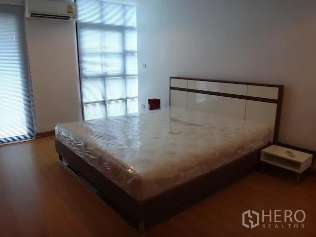 Condominium for rent in Bang Rak, Bangkok - Spacious second bedroom with large windows, air conditioning, wood floors, and a bedside table.