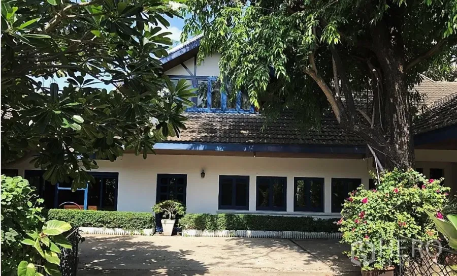 独立式住宅 出租在Khlong Toei, Bangkok - 被大树环绕的独栋房屋外观，山墙屋顶与蓝色窗框。
