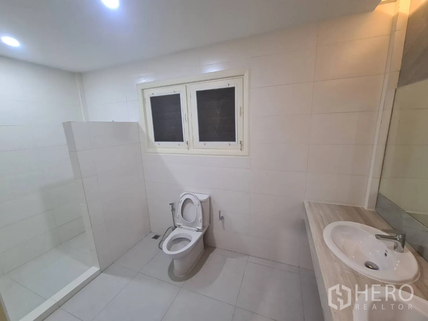 Detached House for rent in Khlong Toei, Bangkok - White tiled bathroom with walk-in shower, toilet and vanity.