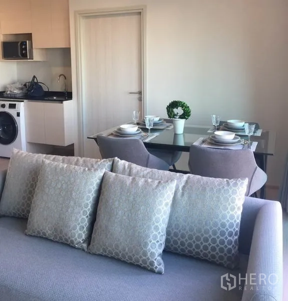 Condominium for rent in Huai Khwang, Bangkok - Open‑plan kitchen with washer and a four‑seat glass dining table beside the sofa.
