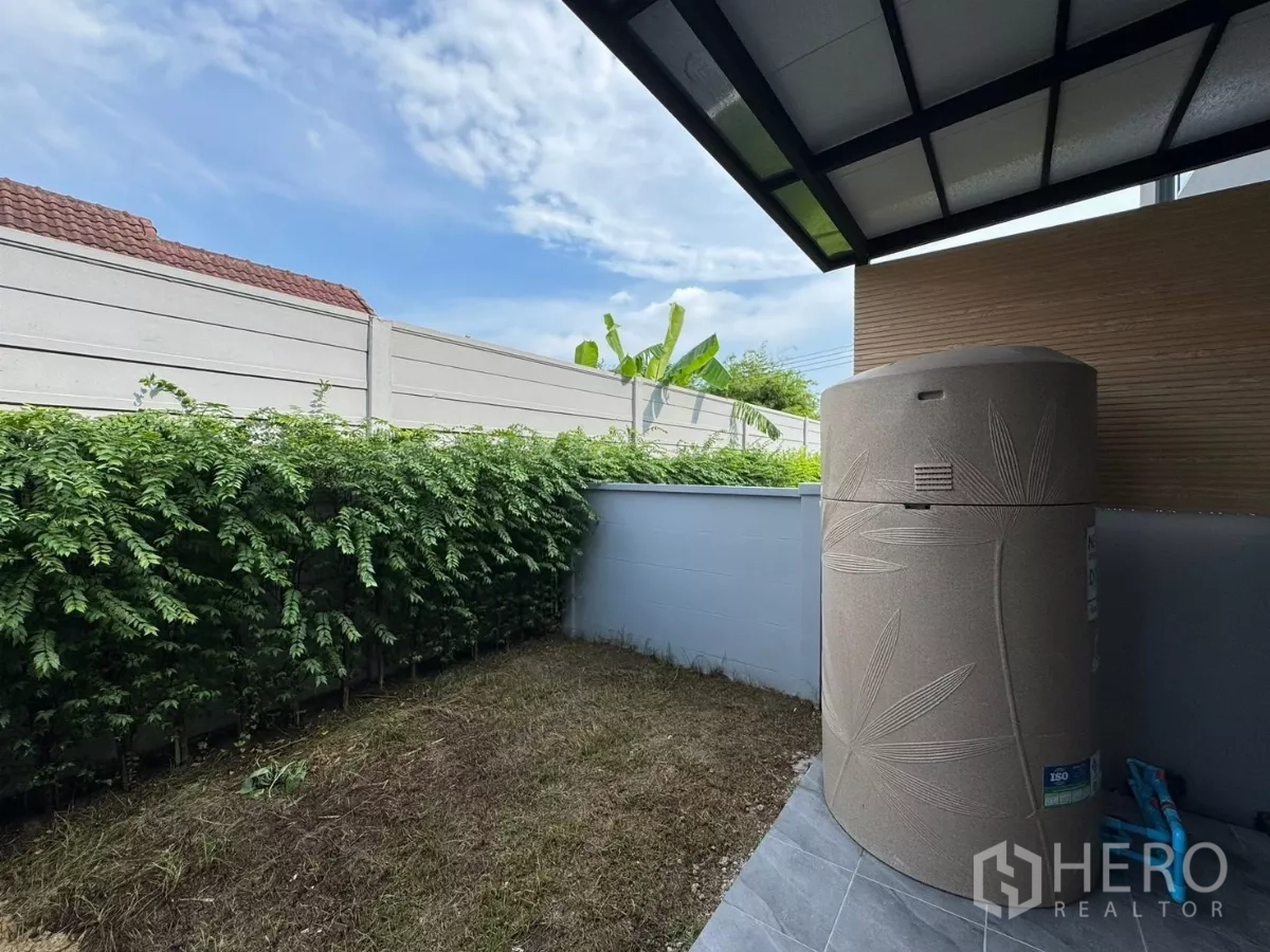 Townhouse for rent in Bang Phli, Samut Prakan - Small backyard lawn with storage water tank under covered area.