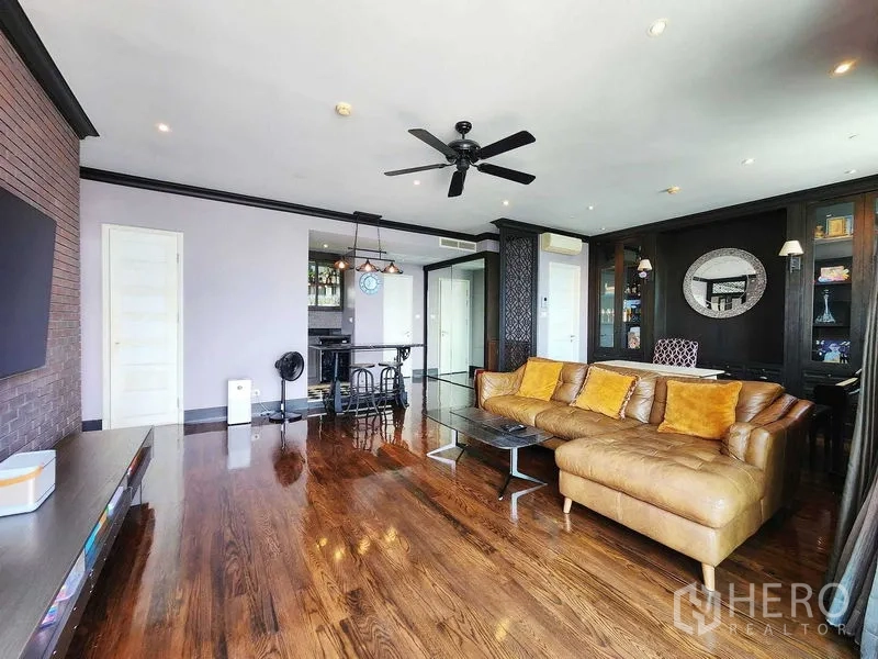 Condominium for sale in Khlong Toei, Bangkok - Open-plan lounge with sectional sofa, ceiling fan and polished hardwood floors.