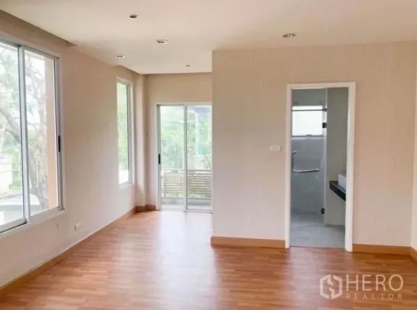Detached House for sale in Saphan Sung, Bangkok - Sunlit living area with corner windows, balcony access and a doorway to the tiled bathroom.