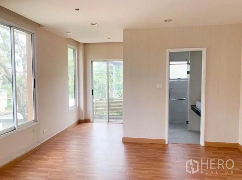 Detached House for sale in Saphan Sung, Bangkok - Sunlit living area with corner windows, balcony access and a doorway to the tiled bathroom.