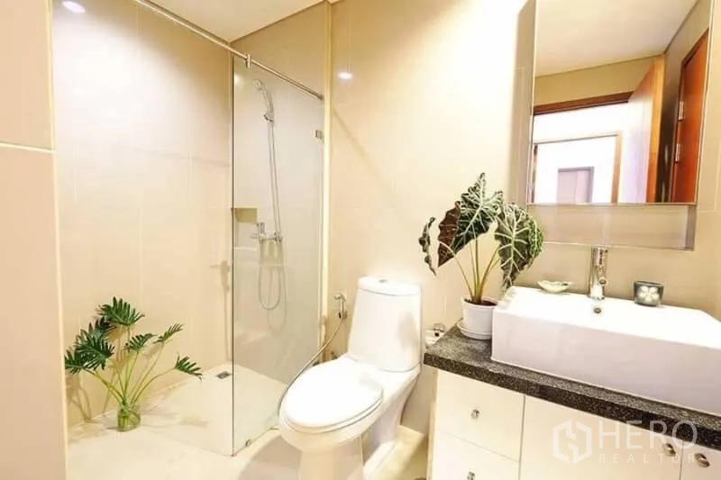 公寓 出租在Khlong San, Bangkok - 明亮浴室，玻璃淋浴间、白色台盆与现代洁具并点缀绿植。