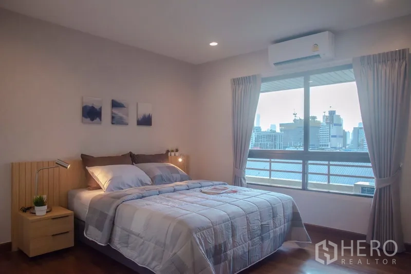 Condominium for rent in Pathum Wan, Bangkok - Second bedroom with double bed, curtains and city skyline outlook.