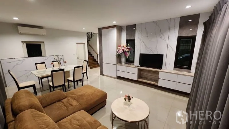 独立式住宅 出租在Prawet, Bangkok - 开放式客餐厅，转角沙发、电视墙与楼梯。