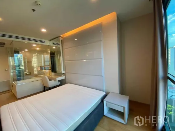 Condominium for rent in Bang Rak, Bangkok - Bright bedroom with glass partition, built-in headboard and desk, city window view.