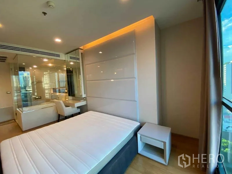 Condominium for rent in Bang Rak, Bangkok - Bright bedroom with glass partition, built-in headboard and desk, city window view.