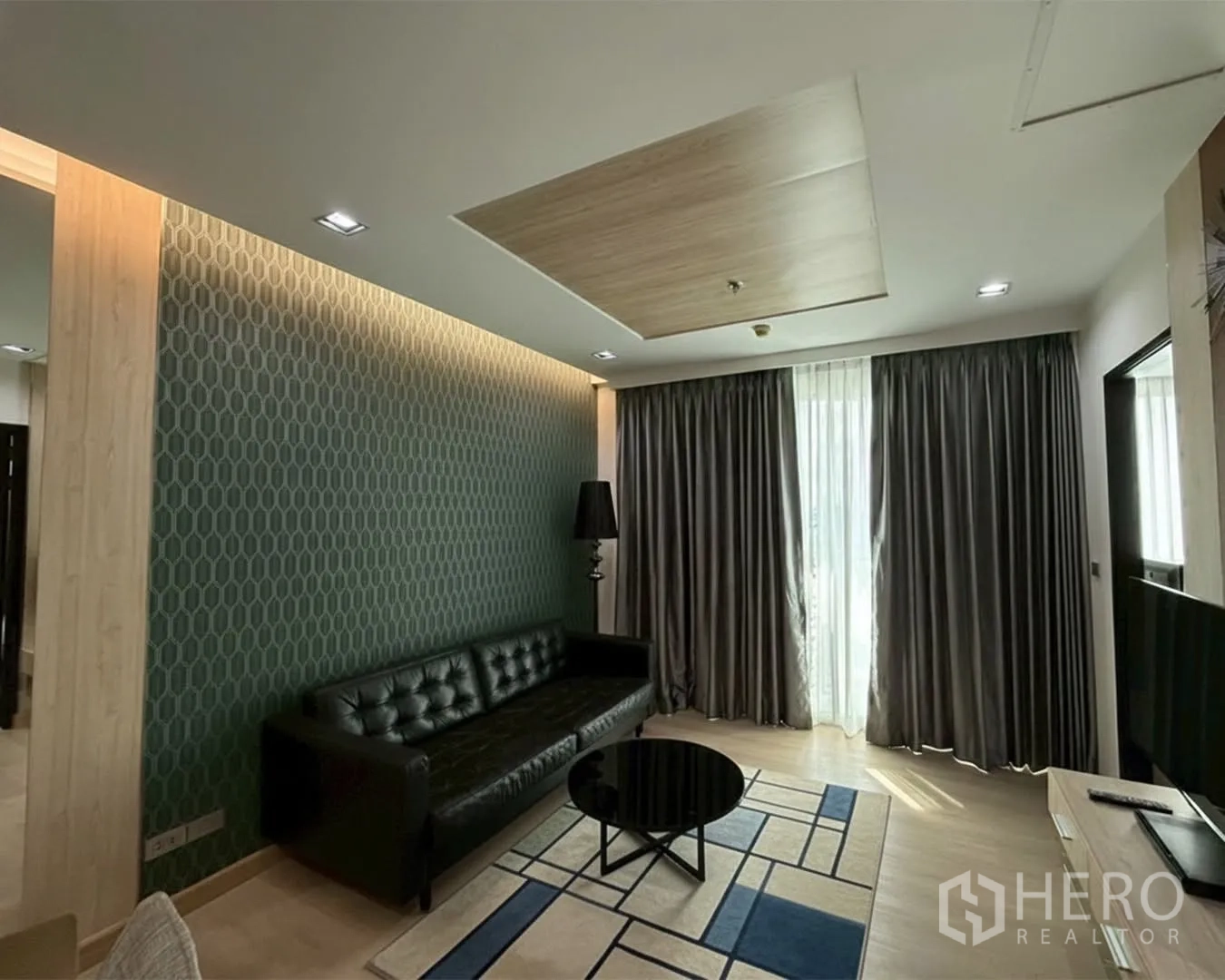 คอนโด for rent or sale in Watthana, Bangkok - ห้องนั่งเล่นโมเดิร์นมีโซฟาหนัง ผนังลาย โต๊ะกลาง และผ้าม่านเต็มความสูง