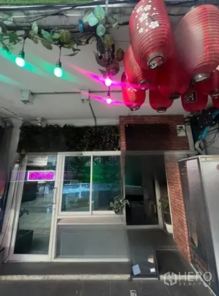 Shophouse for rent in Watthana, Bangkok - Street-front shophouse entrance with glass sliding door, red lanterns, neon OPEN sign and hanging plants near Thonglor BTS in Bangkok.