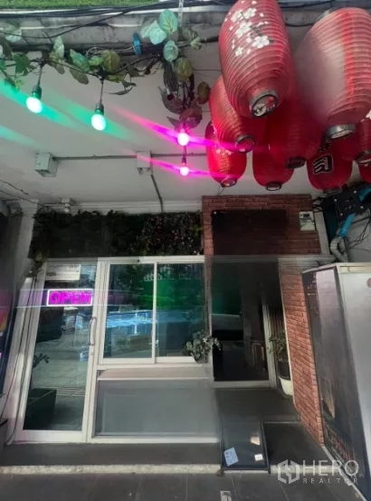 店屋 出租在Watthana, Bangkok - 临街店屋入口，玻璃推门、红色灯笼、霓虹OPEN招牌与绿植，靠近曼谷通罗站。