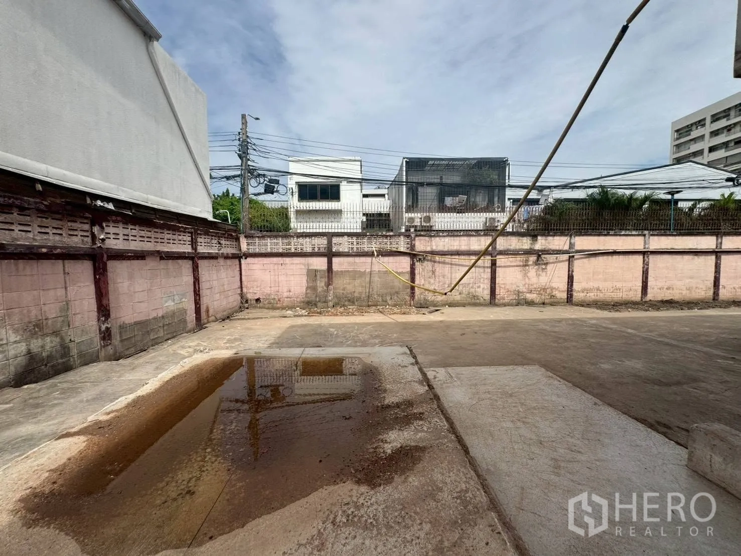 独栋房屋 for rent or sale in Watthana, Bangkok - 围墙内的混凝土院子，可见积水与周边低层建筑。