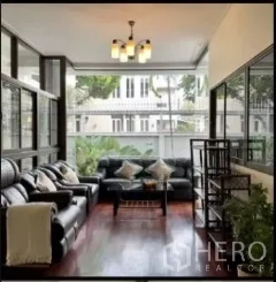 Detached House for rent in Phra Khanong, Bangkok - Enclosed veranda living area with leather sofas and floor-to-ceiling windows.