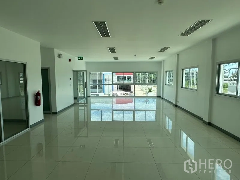 Factory for rent in Mueang Samut Prakan, Samut Prakan - Large office workspace with full-height glazing toward the street and emergency exit signage.