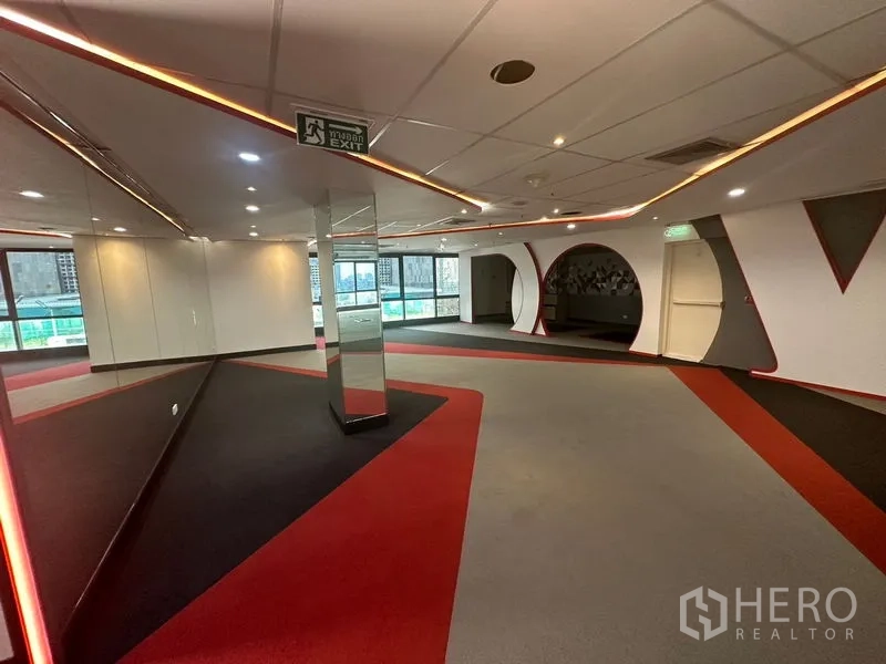 Office Space for rent in Khlong Toei, Bangkok - Reception area with mirrors, exit signage, and red‑gray carpeting beside broad windows.