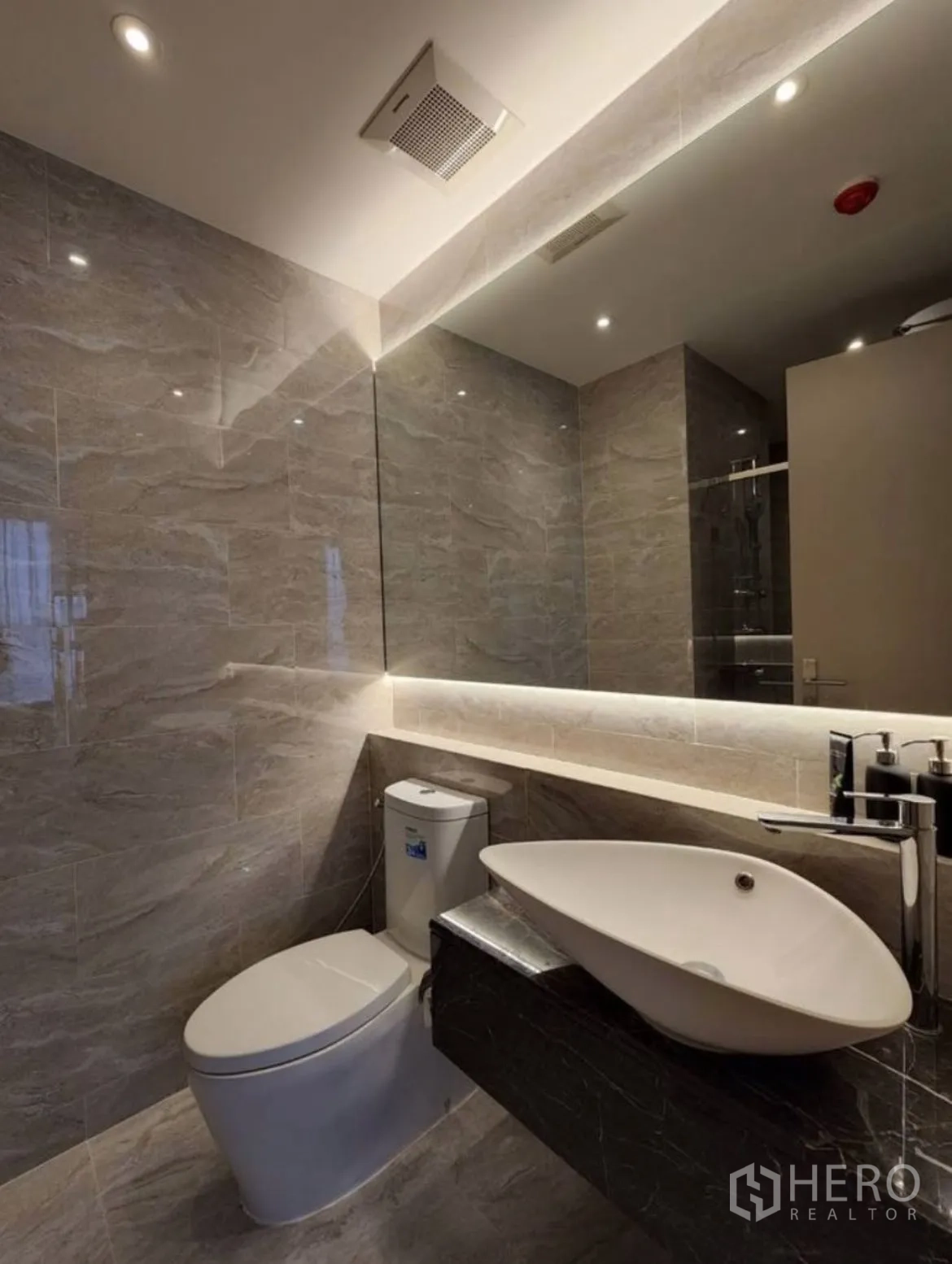 Condominium for rent in Din Daeng, Bangkok - Bathroom vanity with vessel sink, backlit mirror, and stone walls.