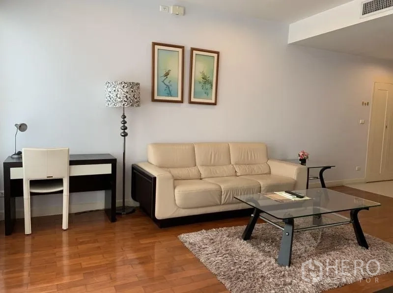 Condominium for rent in Khlong Toei, Bangkok - Living area with cream sofa, work desk, floor lamp and glass coffee table on a rug.