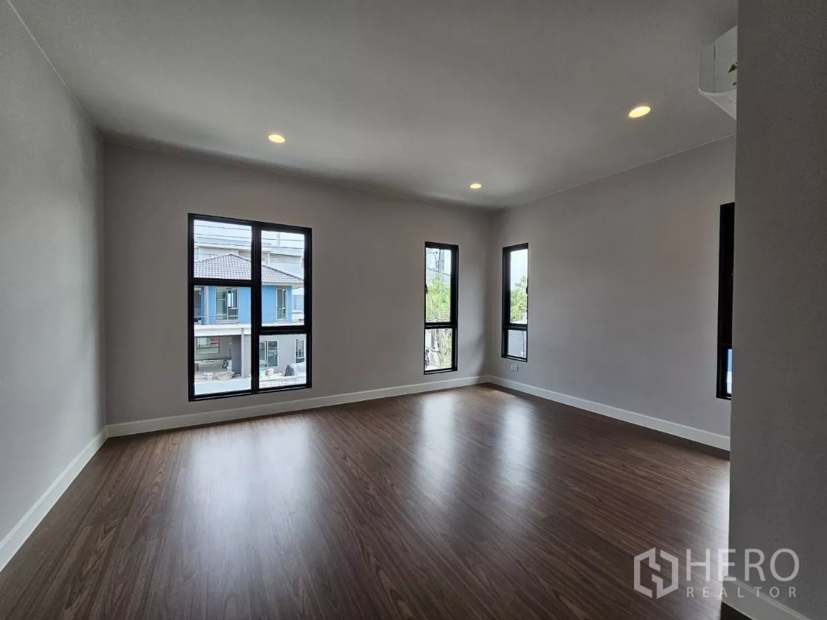 Detached House for sale in Lam Luk Ka, Pathum Thani - Spacious master bedroom with multiple windows and wood floors.