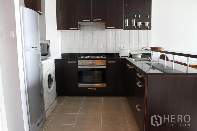Apartment for rent in Bang Rak, Bangkok - Modern kitchen with dark wood cabinets, built-in oven, fridge and washing machine.