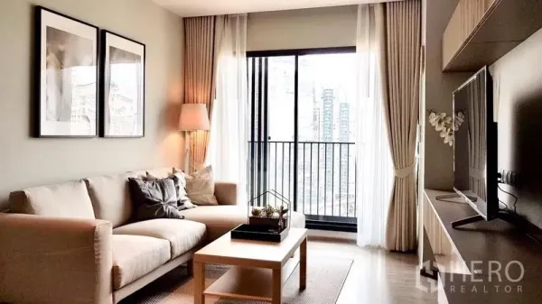 Condominium for rent in Watthana, Bangkok - Living room opening to a balcony with city skyline view and TV wall unit.