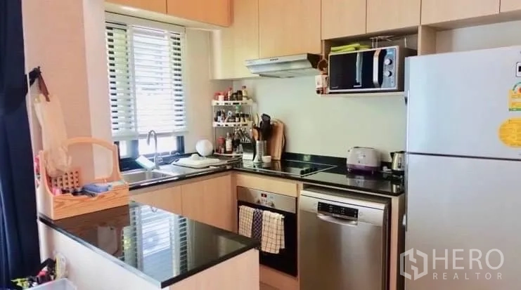 Townhouse for rent or sale in Suan Luang, Bangkok - L-shaped kitchen with light wood cabinets, black countertops and modern appliances.