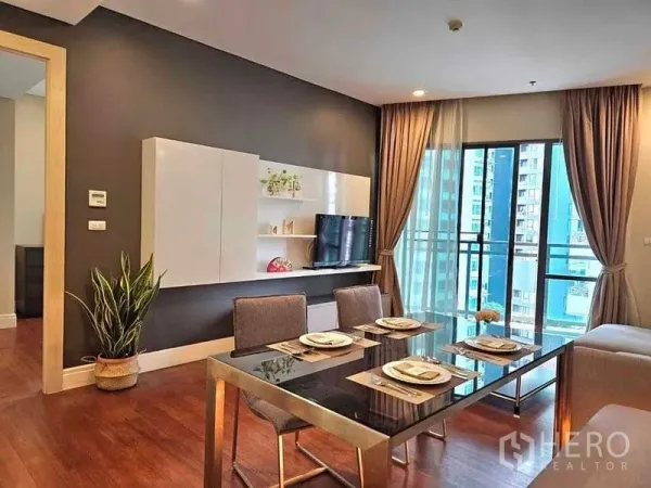Condominium for rent or sale in Khlong Toei, Bangkok - Contemporary living and dining area with glass-top table, TV wall unit and balcony doors overlooking the city.