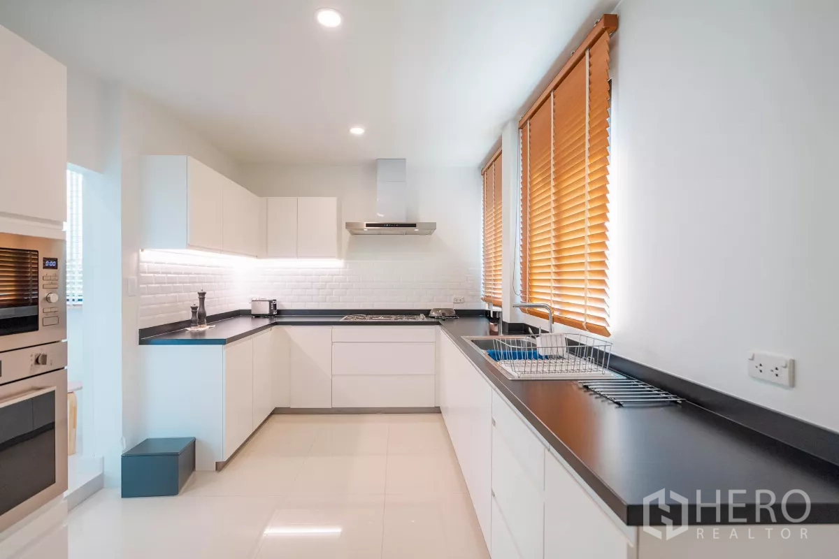 Detached House for sale in Saphan Sung, Bangkok - Modern U-shaped kitchen with white cabinetry, black countertops and windows.