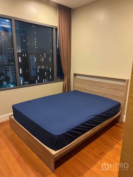 Condominium for rent in Khlong Toei, Bangkok - Cozy bedroom with queen bed, wood floors, curtains and nighttime city window view.